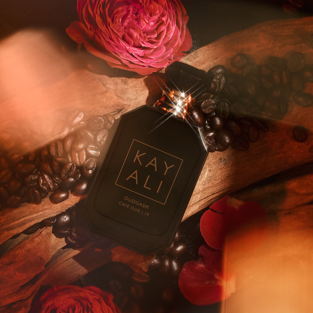Black perfume bottle labeled 'KAY ALI' with coffee beans and roses on a wooden surface.