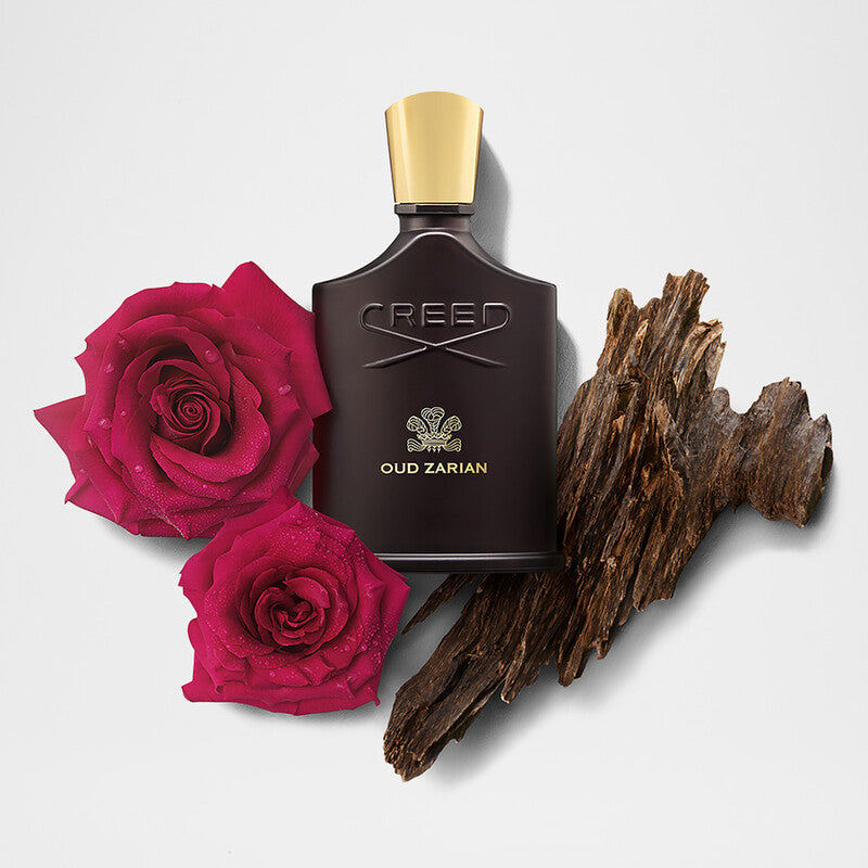 Creed Oud Zarian perfume bottle with pink roses and wooden element on a light gray background