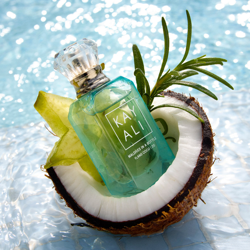 Green perfume bottle labeled 'KAY ALI' on a coconut with a blue water background