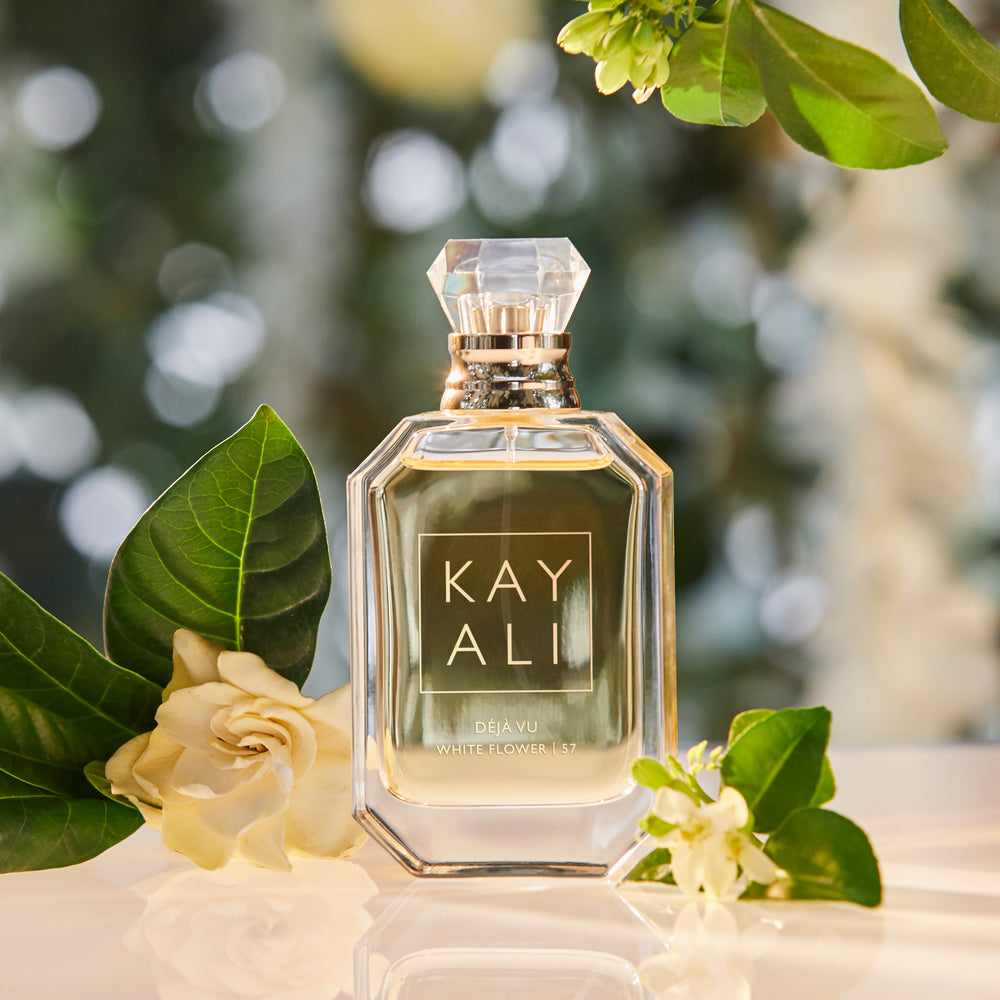 Perfume bottle labeled 'KAYALI' with flowers and green leaves on a blurred natural background