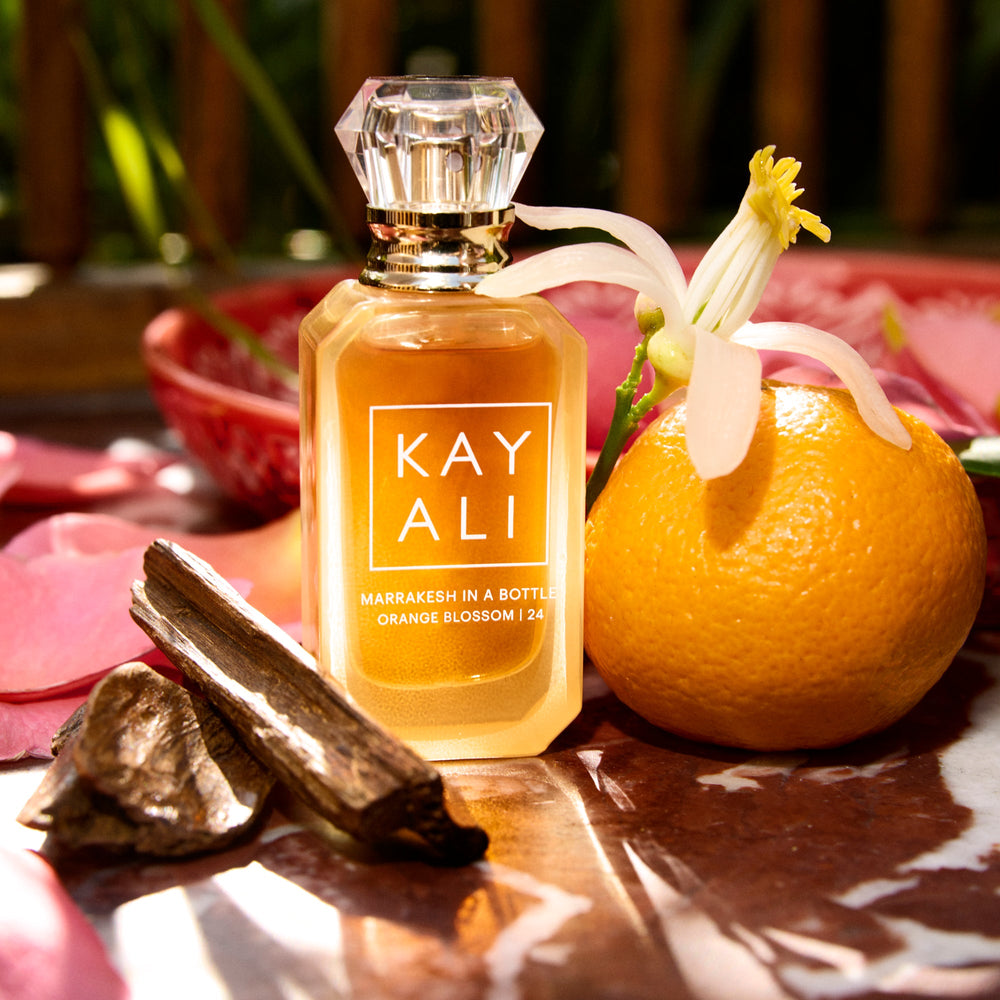 Perfume bottle labeled 'KAY ALI' with an orange and floral elements on a reflective surface.