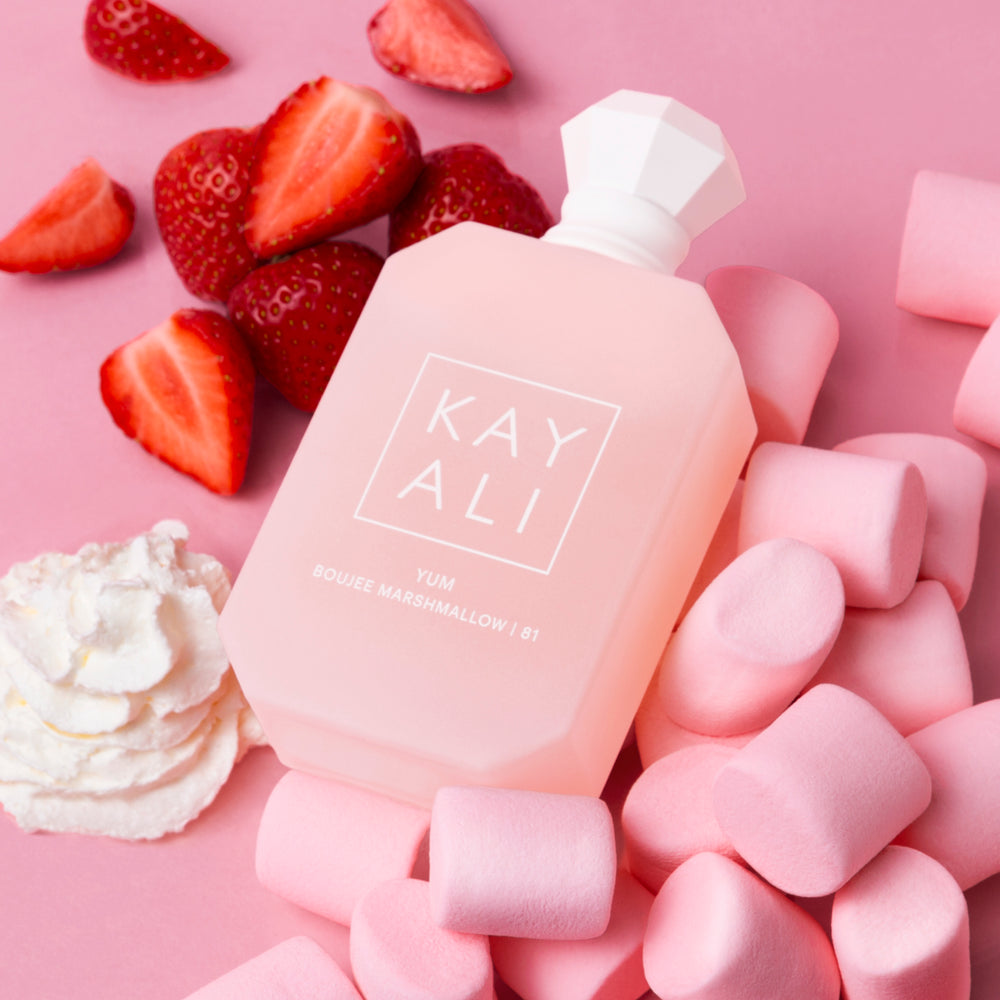 Pink bottle labeled 'KAY ALI' surrounded by strawberries, marshmallows, and whipped cream on a pink background