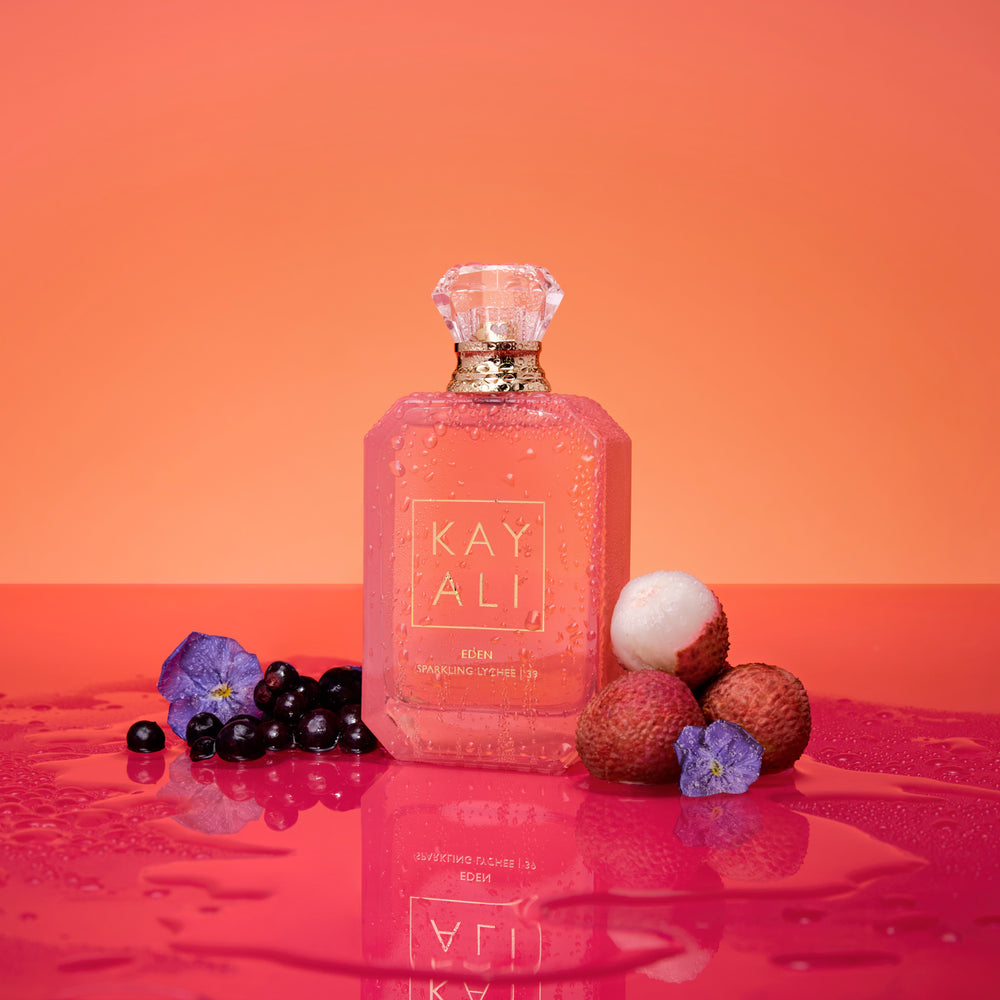 Pink bottle of KAY ALI perfume with lychees and berries on a red surface and orange background