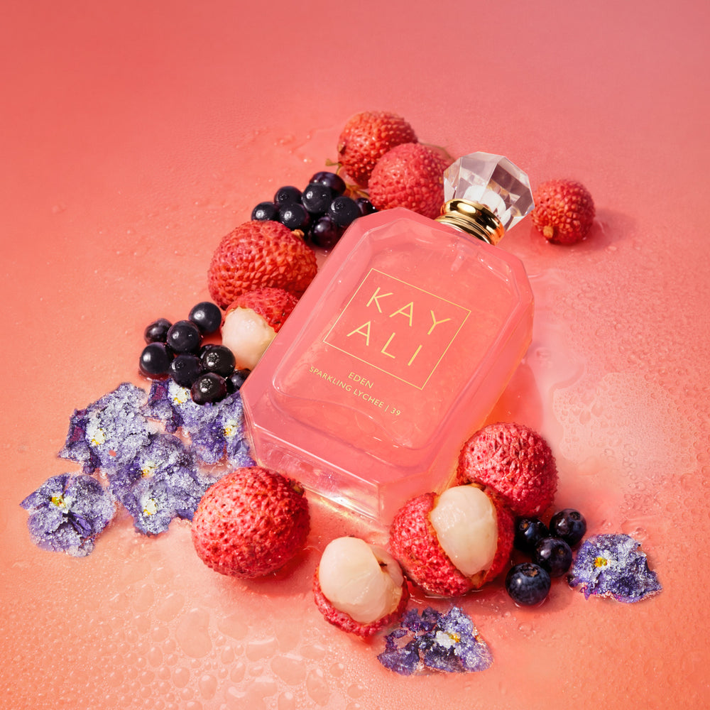 Pink perfume bottle with berries and flowers on a pink background