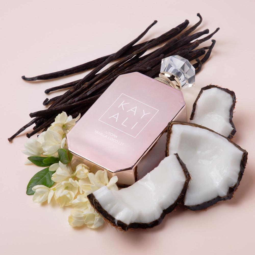 Pink perfume bottle with vanilla beans, coconut pieces, and flowers on a pink background