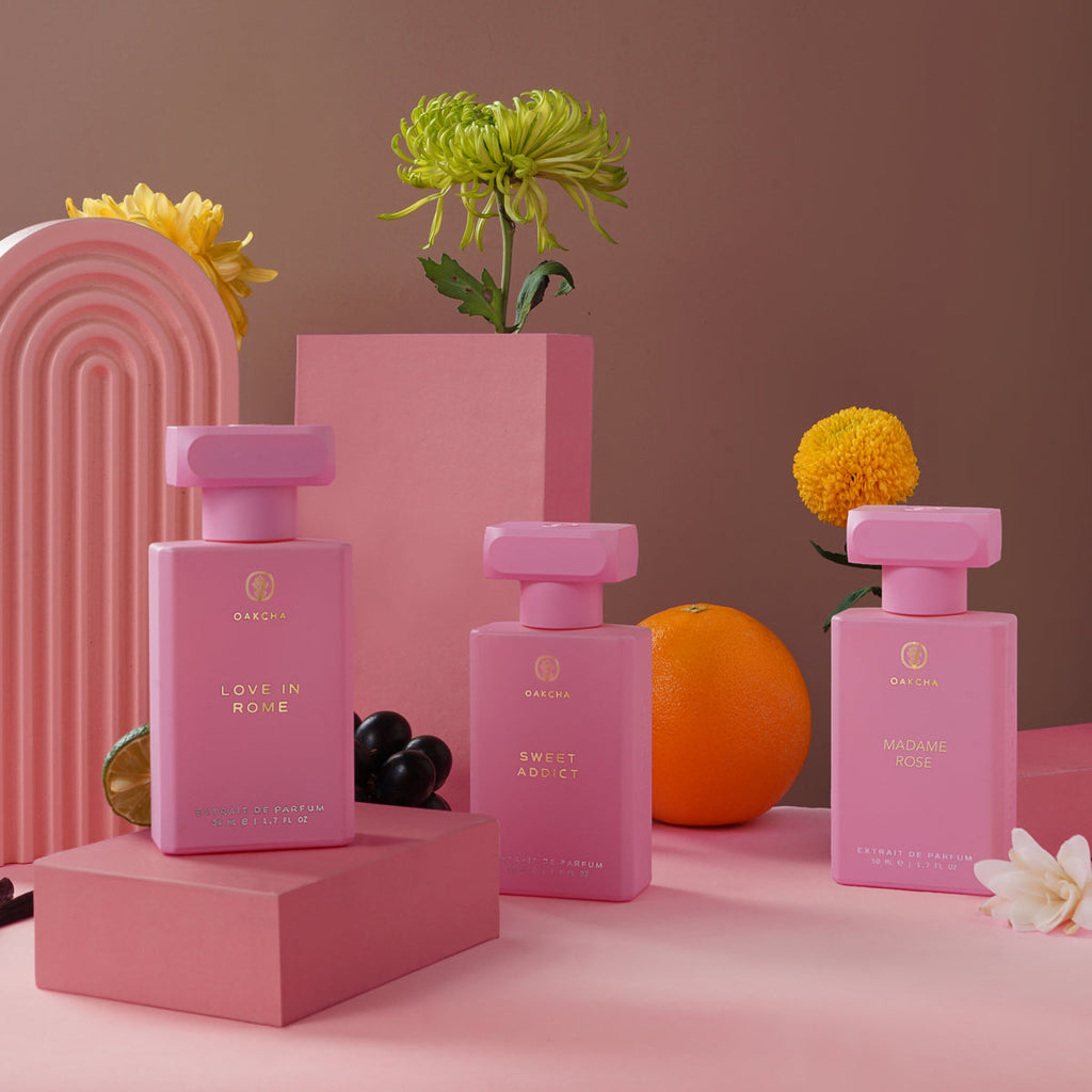 Three pink perfume bottles on pink stands with flowers and fruits against a pink background