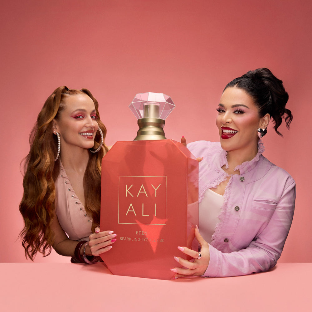 Two women holding a large red 'KAY ALL' product against a pink background