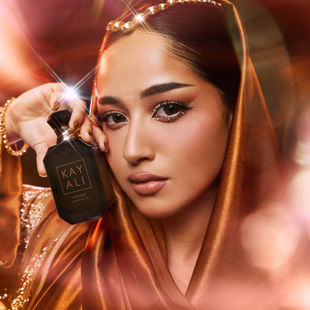 Woman holding a black perfume bottle labeled 'KAY ALI' with a warm, glowing background.