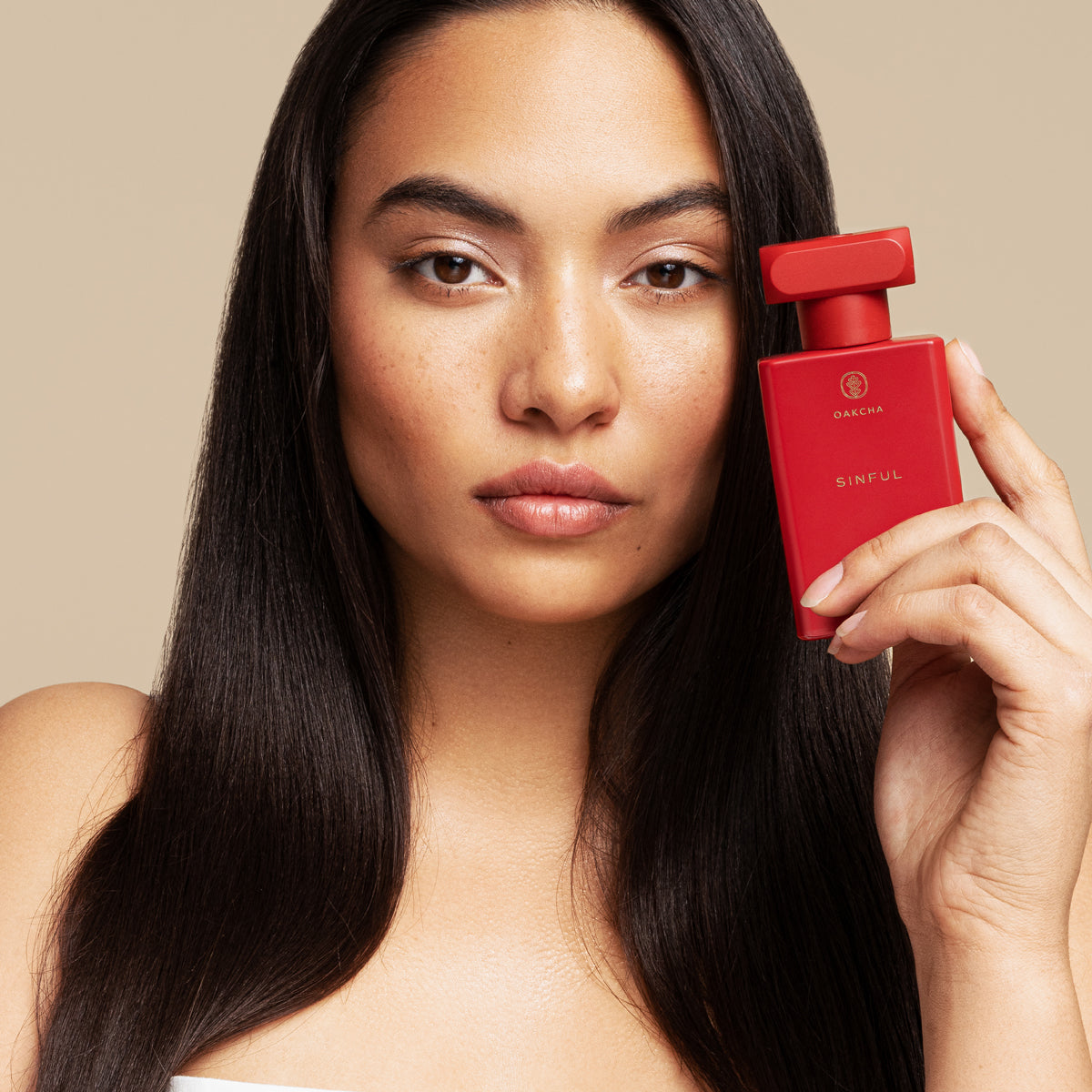 Woman holding a red perfume bottle against a beige background