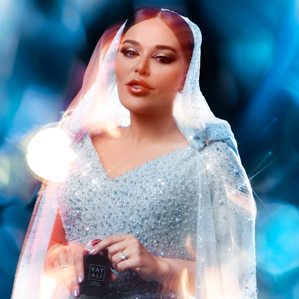 Woman in a sparkling outfit holding a product with 'KAYALI' branding against a blue blurred background